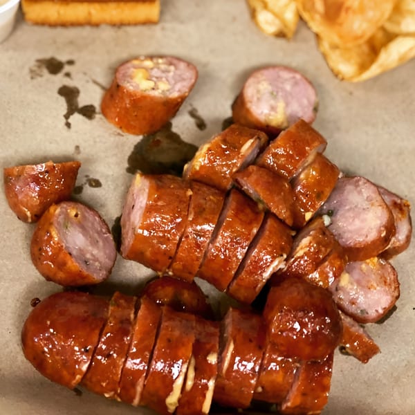 Sliced smoked sausage with cheese and herbs, glistening with sauce, on a brown paper surface.