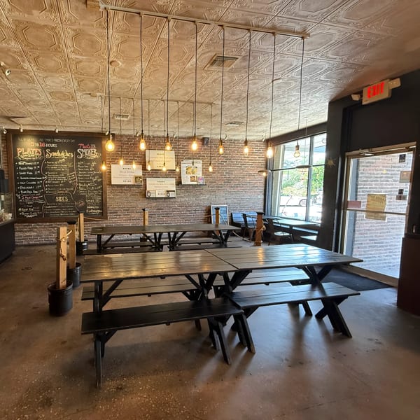 Interior of Smoke BBQ restaurant with long wooden picnic tables, brick walls, and a large menu chalkboard.