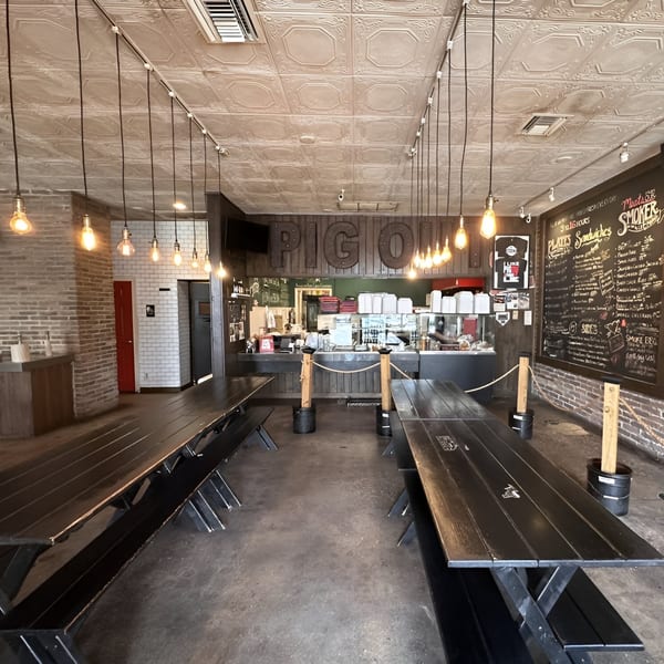 Interior of Smoke BBQ restaurant with long black picnic tables, brick walls, and a counter.