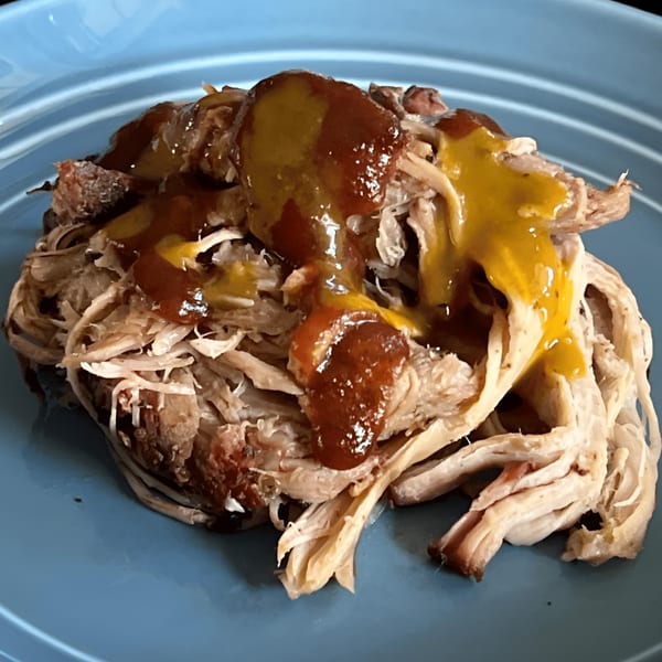 Close-up of Smoke BBQ's pulled pork on a blue plate, topped with barbecue and mustard sauces.