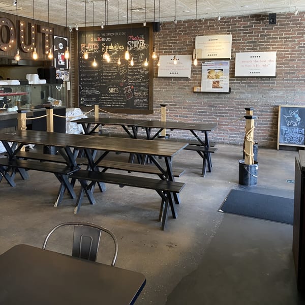 Interior of Smoke BBQ restaurant with long picnic tables, brick walls, and a large chalkboard menu.