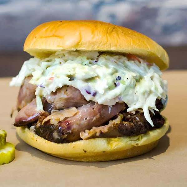 A Smoke BBQ pulled pork sandwich with creamy coleslaw and pickles on a bun.