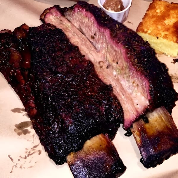 Smoke BBQ's beef ribs with a dark, crispy bark and a pink smoke ring, served with cornbread.