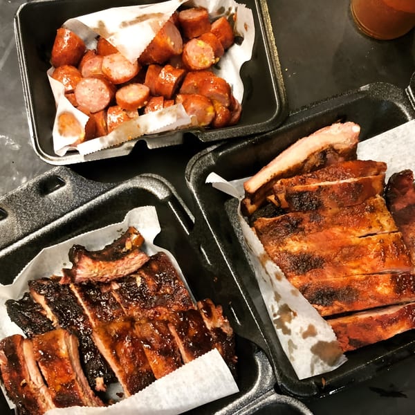 Three black takeout containers filled with Smoke BBQ's sliced ribs and sausage.